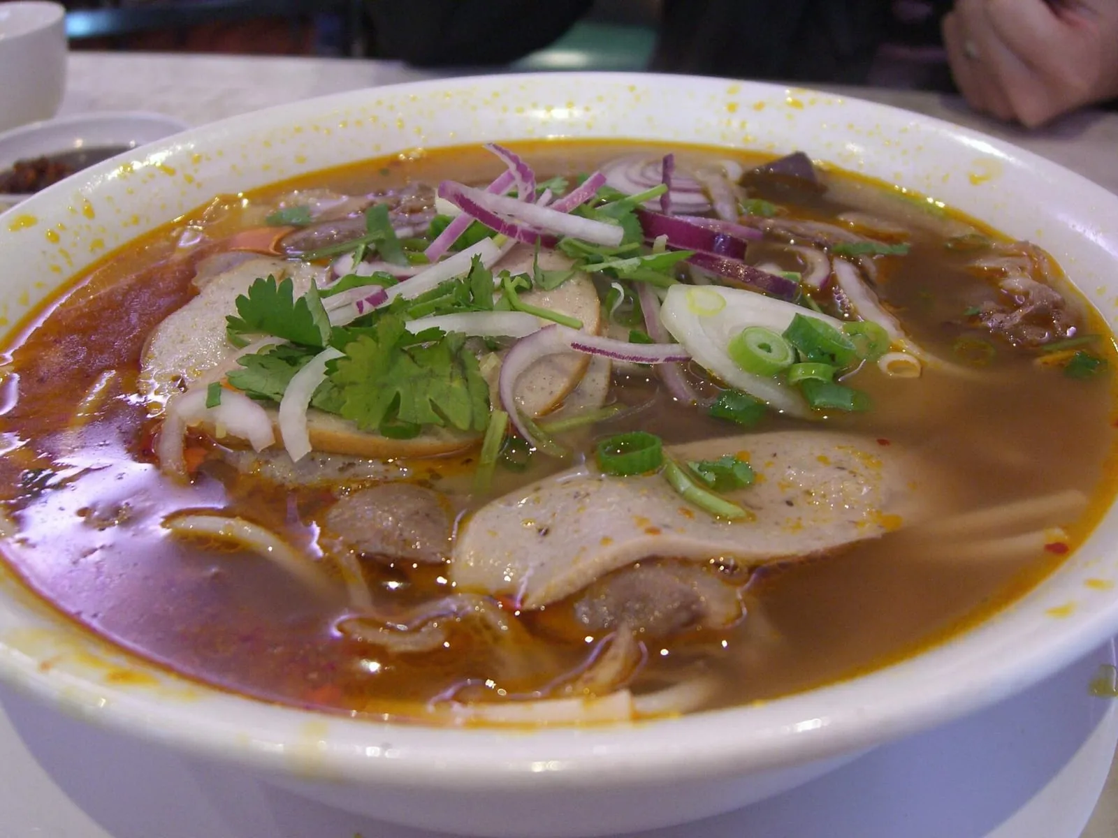 Bún Bò Huế mit roter, scharfer Brühe, Zwiebeln und Kräutern